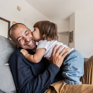 A father receives a kiss on the cheek from his toddler.